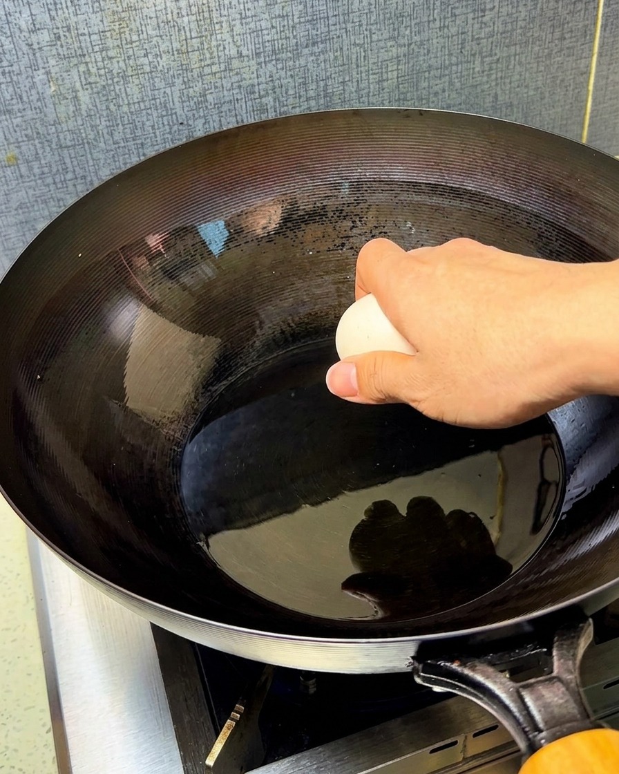 Two raw eggs being dropped into a seasoned, hot wok filled with shimmering cooking oil.