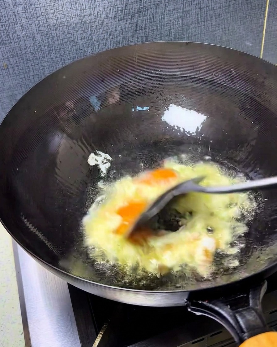 Eggs being scrambled rapidly in a hot wok with a spatula, creating fluffy, golden pieces.