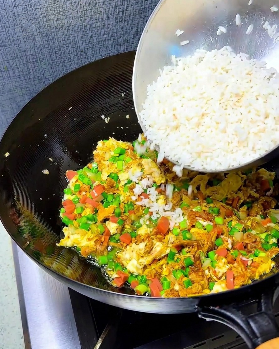 Crumbled white rice being added to the wok containing the stir-fried eggs and vegetable mixture.
