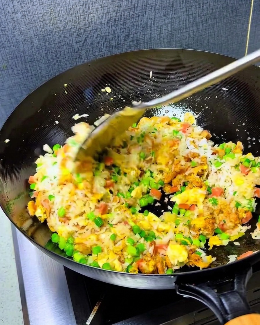 A spoonful of vibrant red chili oil being added to the rice mixture in the hot wok.