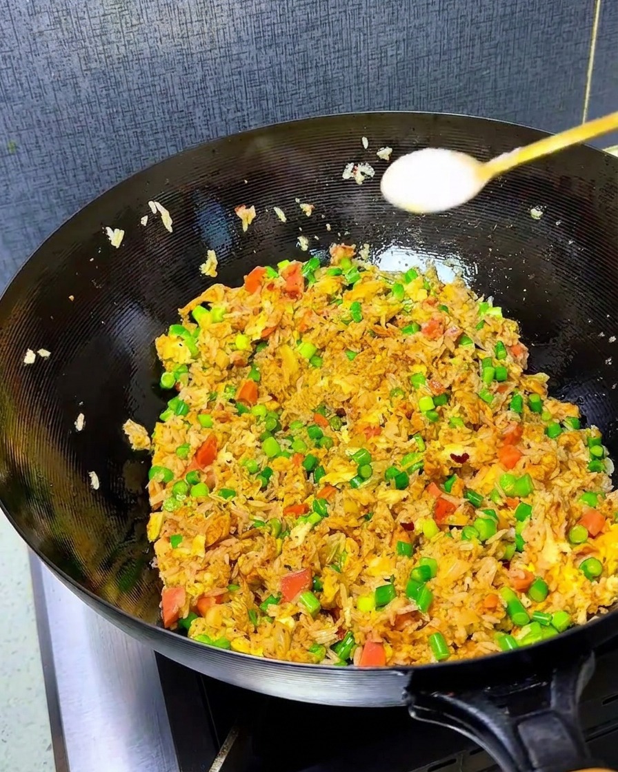 Close-up of salt and chicken bouillon being sprinkled into a wok filled with colorful kimchi fried rice.