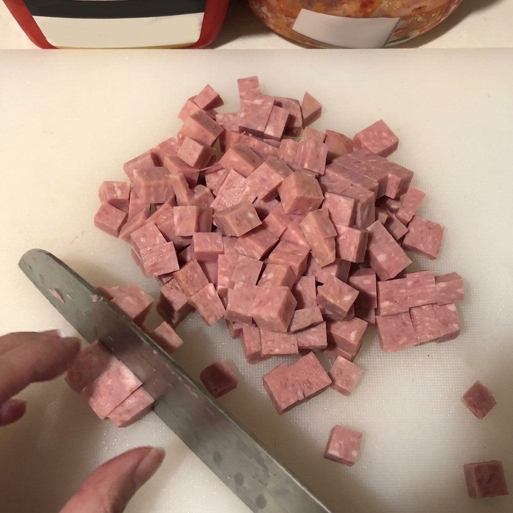 A close-up shot of spam being neatly cubed on a white surface, with a knife blade visible.