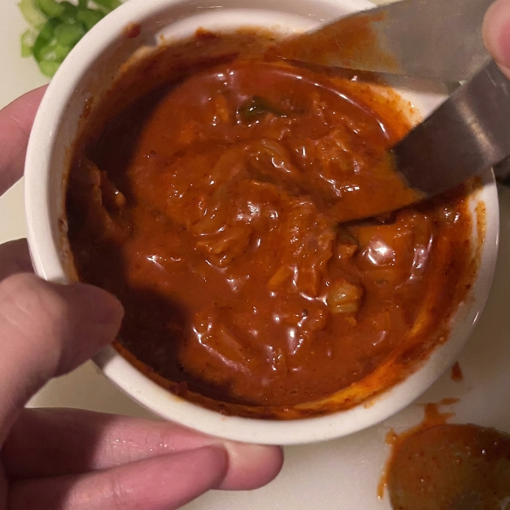 A pair of scissors snipping kimchi pieces directly inside a bowl of sauce.