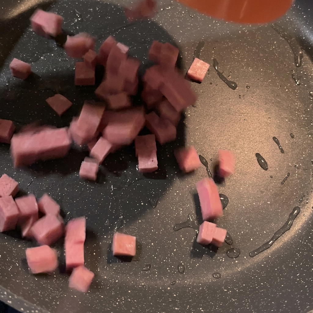 Cubed spam pieces sizzling and browning in a hot pan.