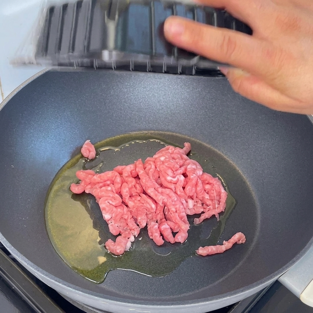 Minced pork being added to a pan with hot oil and stir-fried using a wooden spatula.