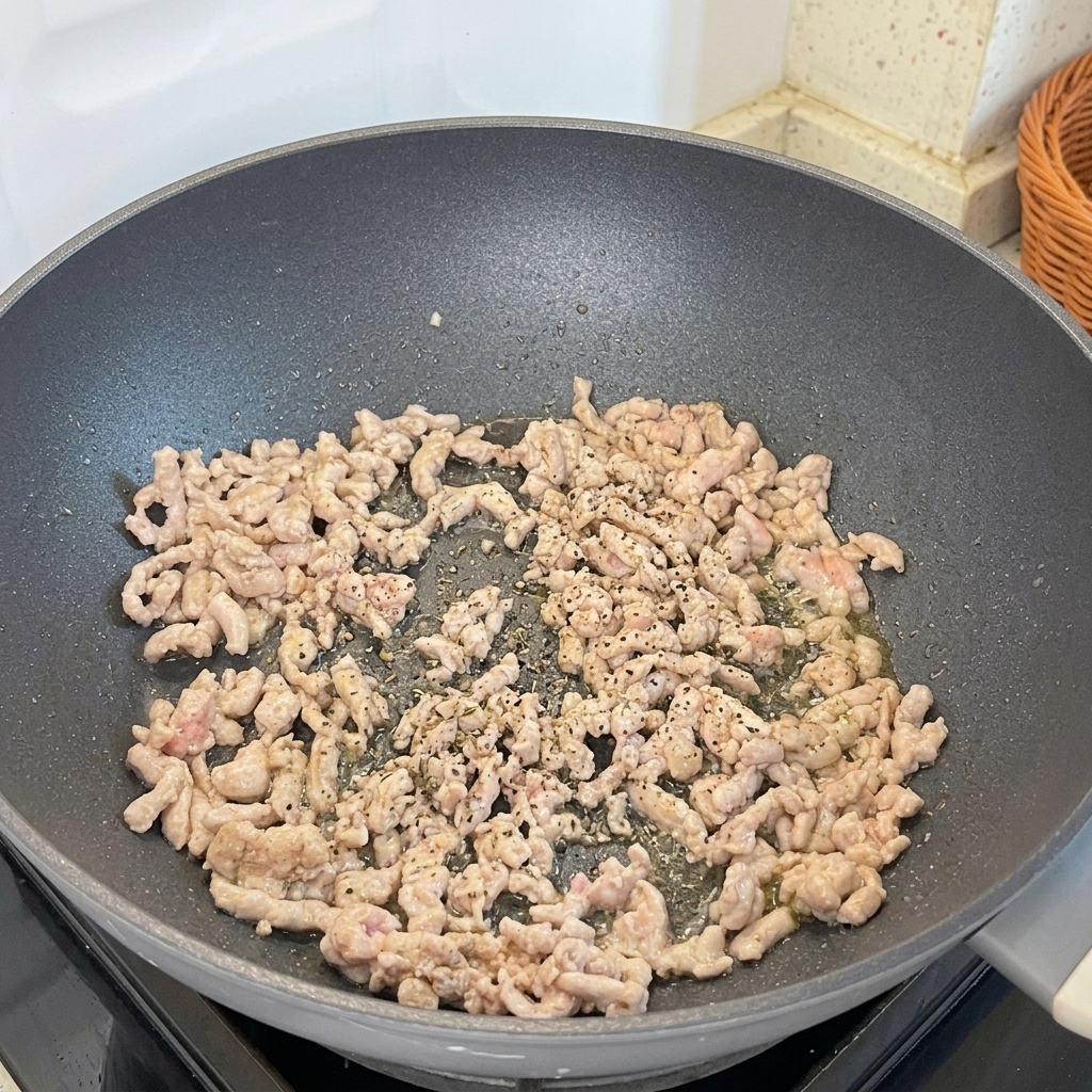 Freshly ground black pepper being added to the browning minced pork in a stir-fry pan.