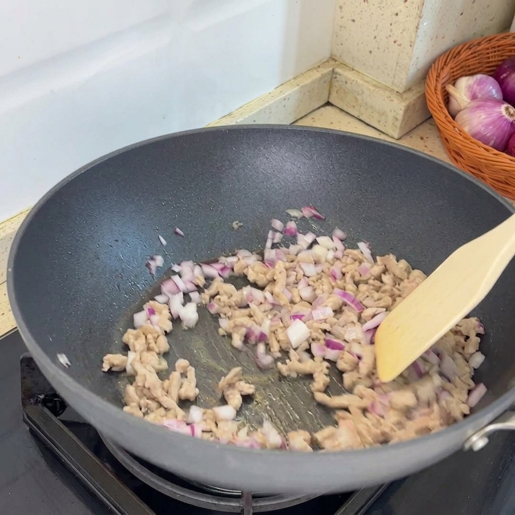 Chopped shallots being added to the pan and combined with the cooked minced pork.