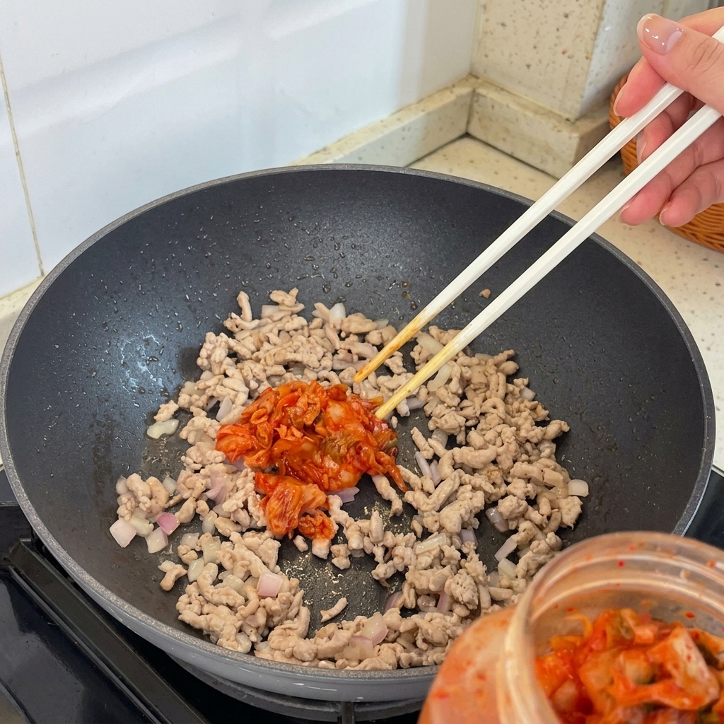 Kimchi pieces being added to the stir-frying meat and shallot mixture in the pan.