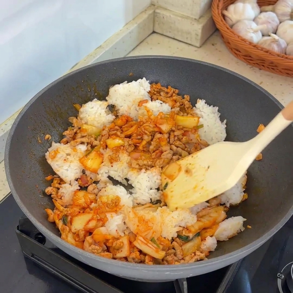 A spatula vigorously tossing the combined rice meat and kimchi mixture in a hot wok.