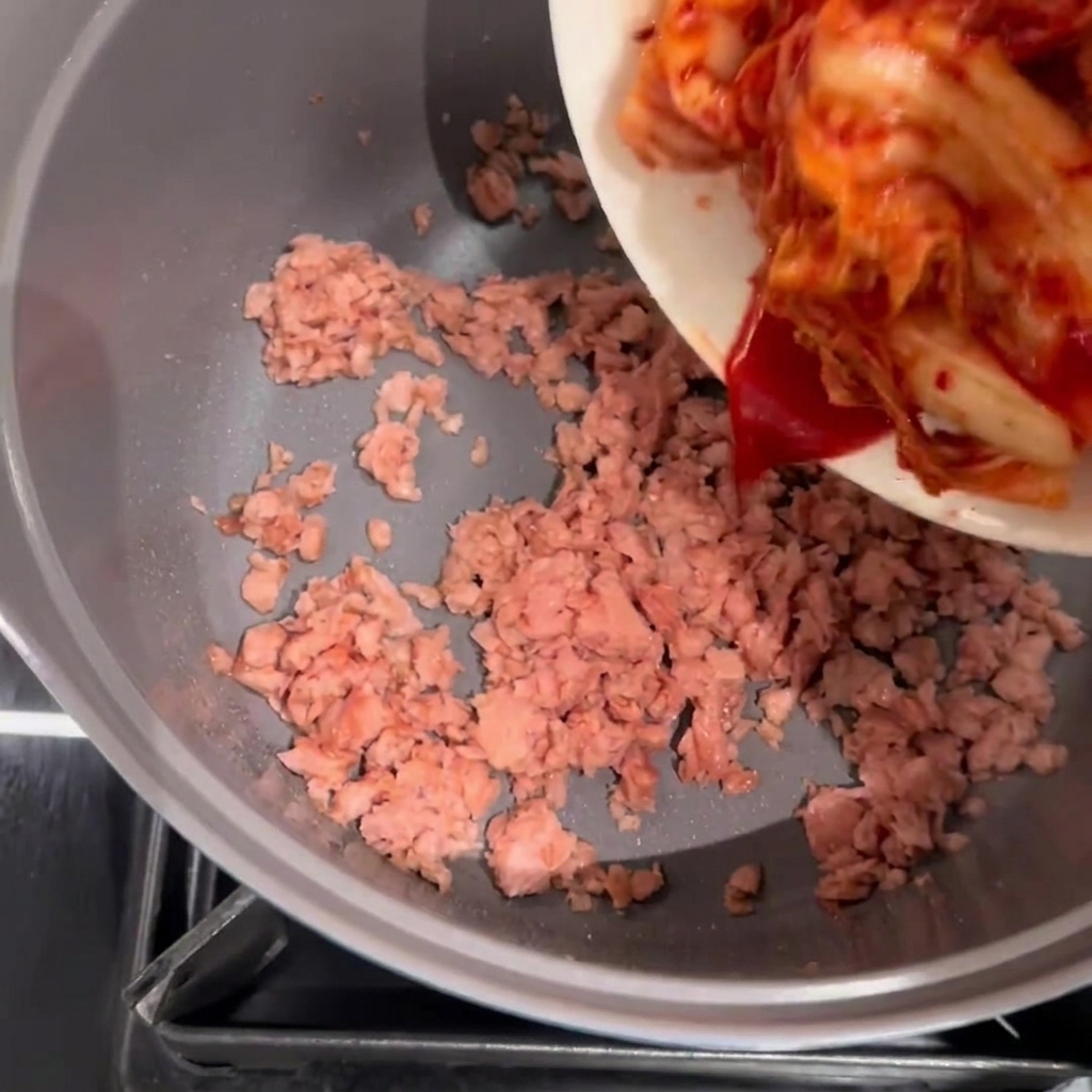 Kimchi being added to a pot of browned, stir-fried Spam.
