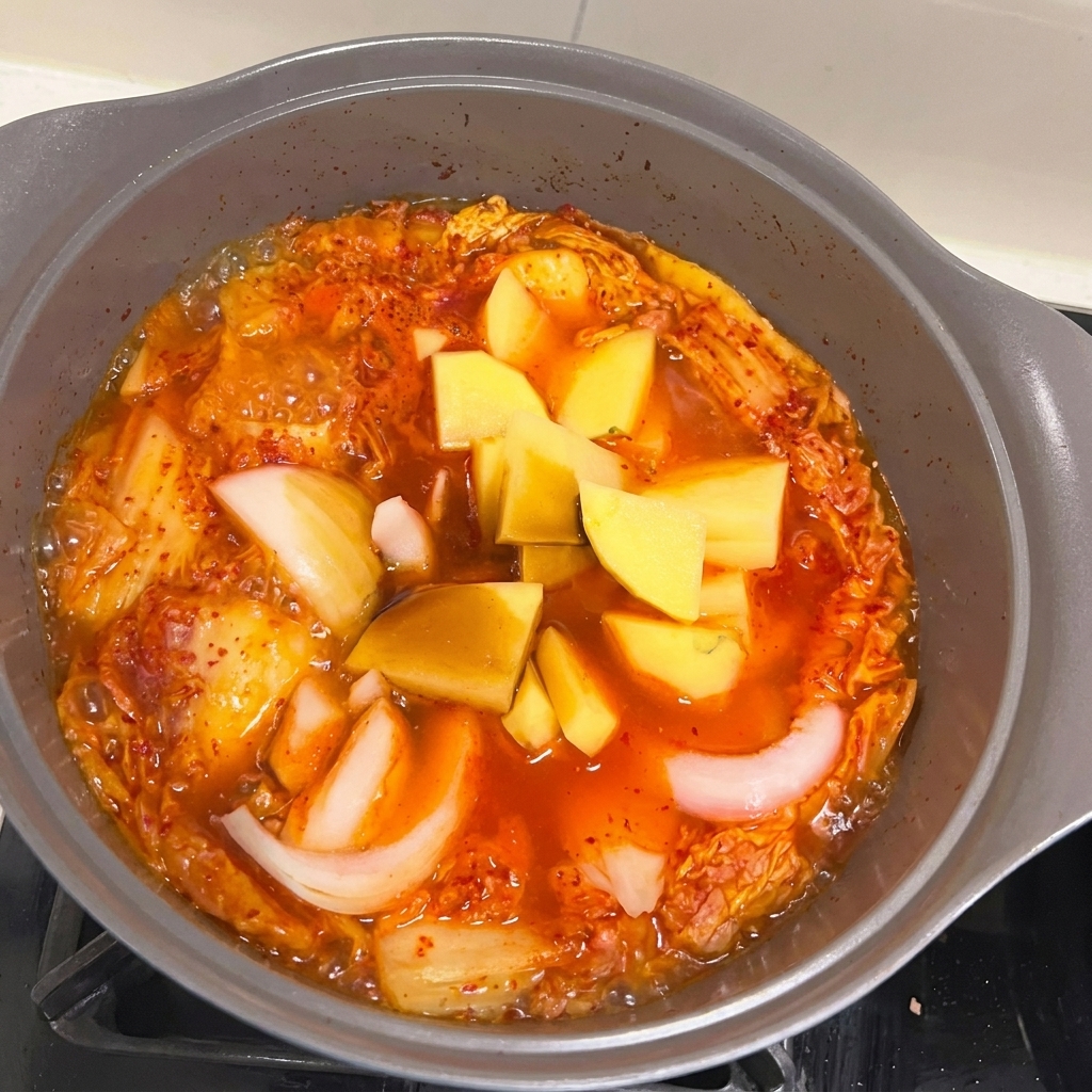 Chopped pieces of onion and potato being added to the bubbling Spam and kimchi stew.