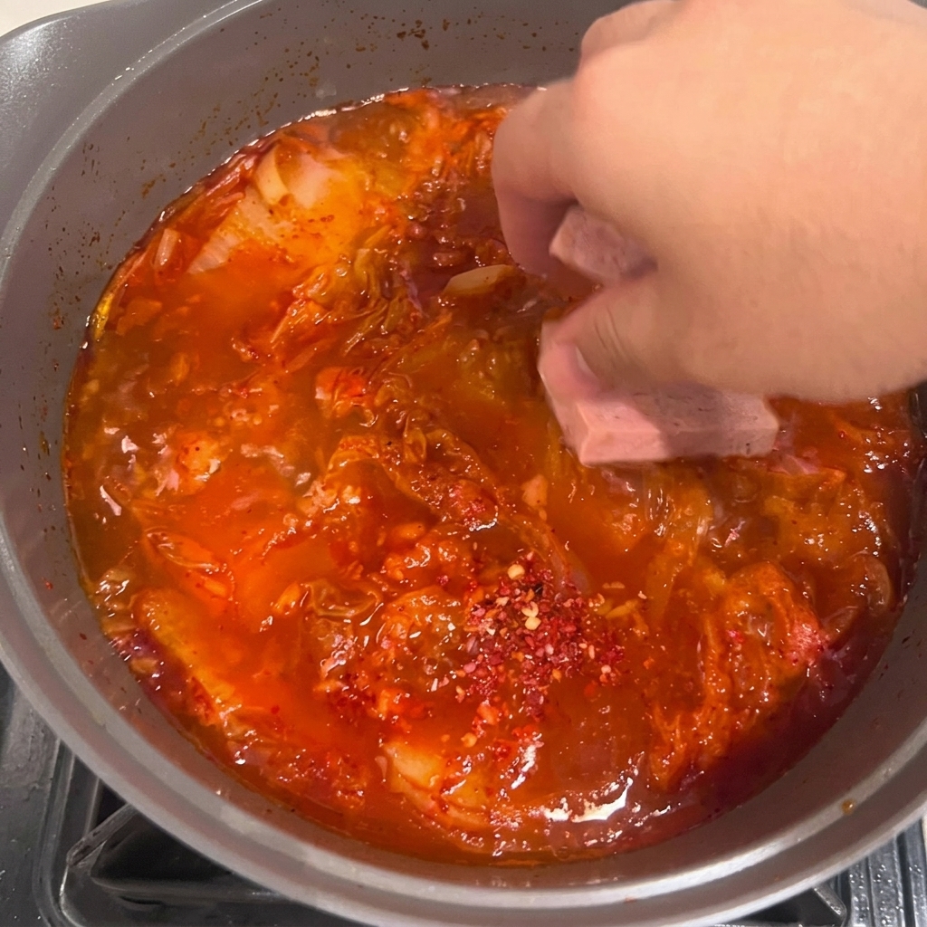 Tofu slices being carefully placed into the bubbling red kimchi stew.