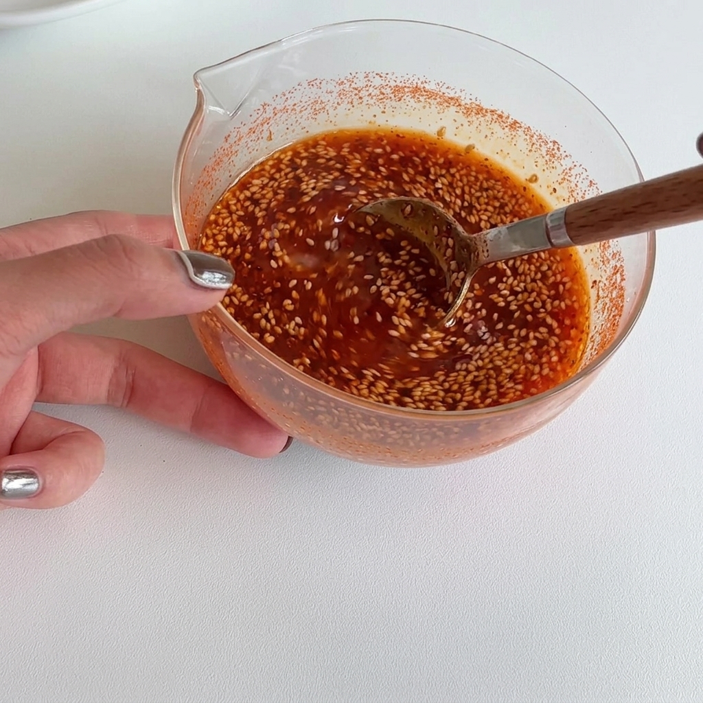 Hand stirring a vibrant, smooth red sauce in a glass bowl with a wooden spoon until perfectly combined.