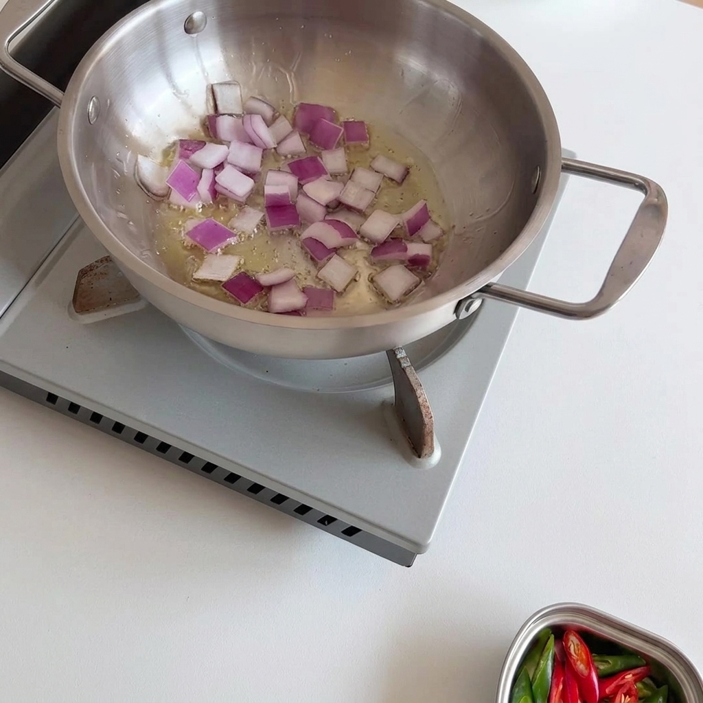 Diced purple onions sizzling and softening in hot oil within a stainless steel pan, being stirred with a wooden spoon.