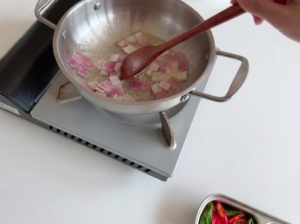 A fresh, even layer of white enoki mushrooms placed carefully over the sautéed onions in the stainless steel pan.