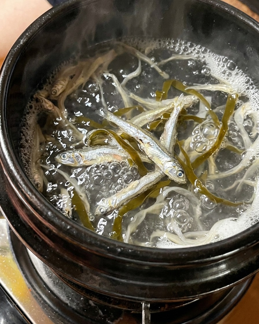 Dried small silver fish and pieces of kelp boiling in a pot of water.