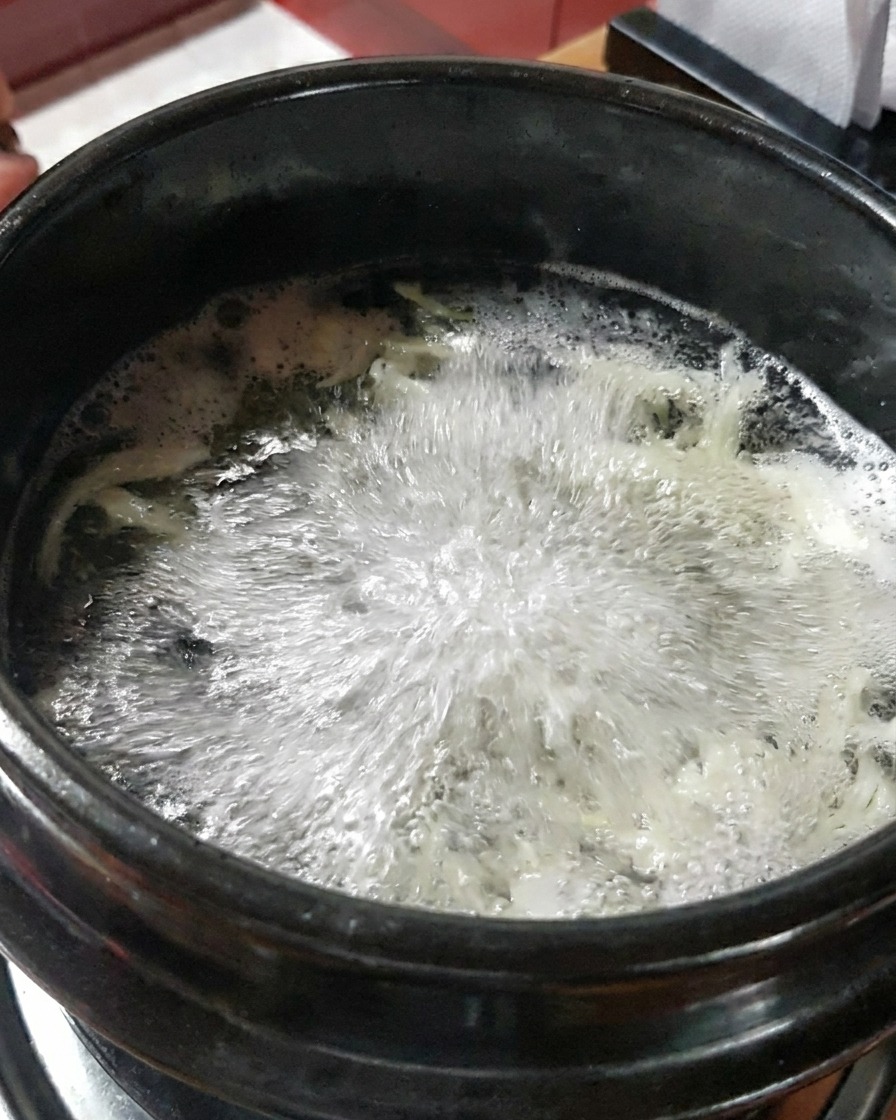 Translucent raw shrimp being poured into the bubbling seafood broth.