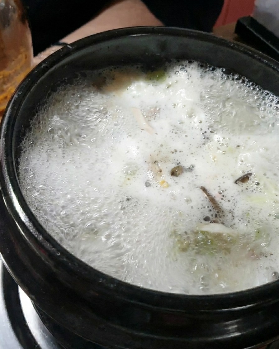 A large spoonful of thick dark soybean paste being stirred into the boiling broth.