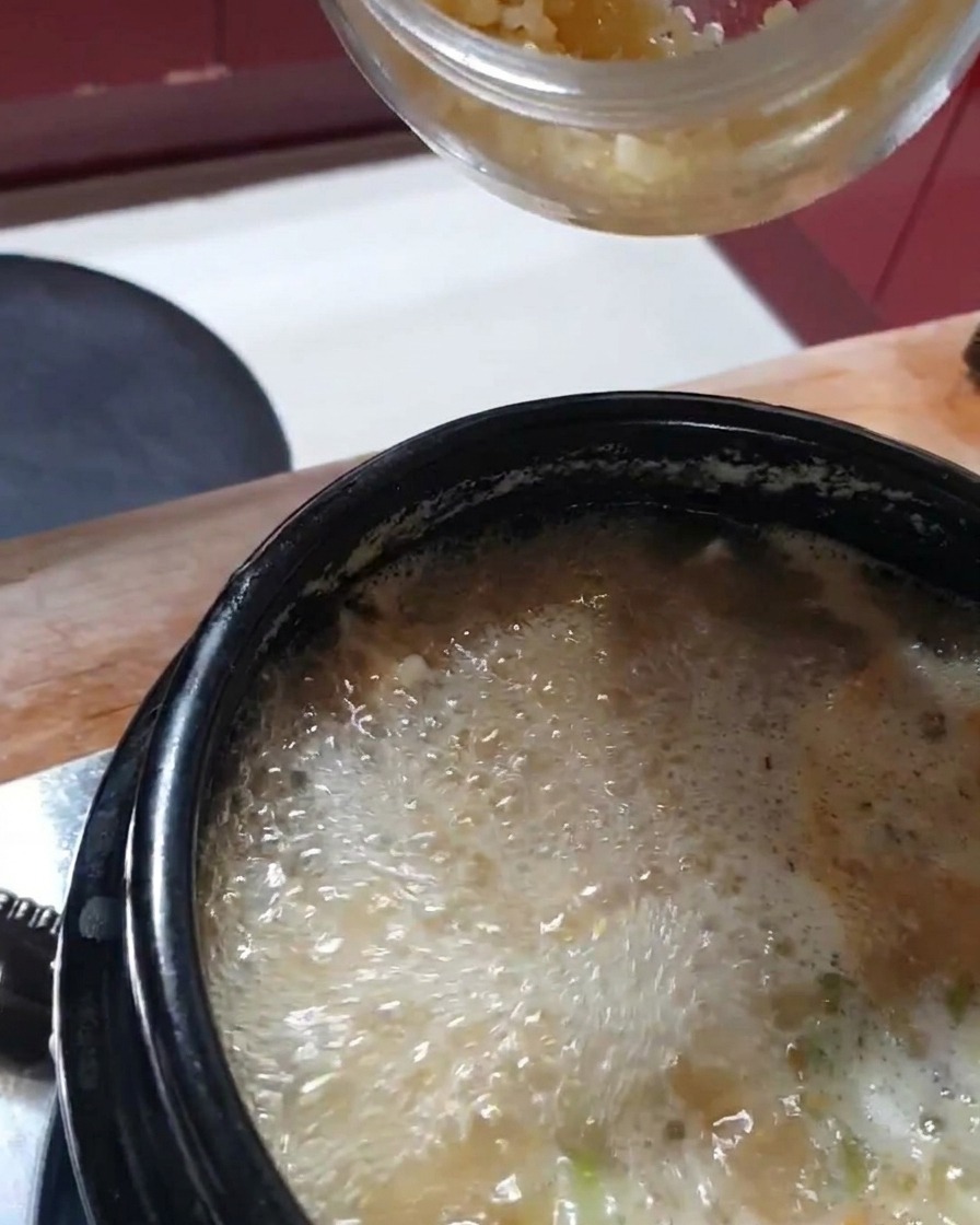 A spoonful of freshly minced garlic being added to the bubbling stew.