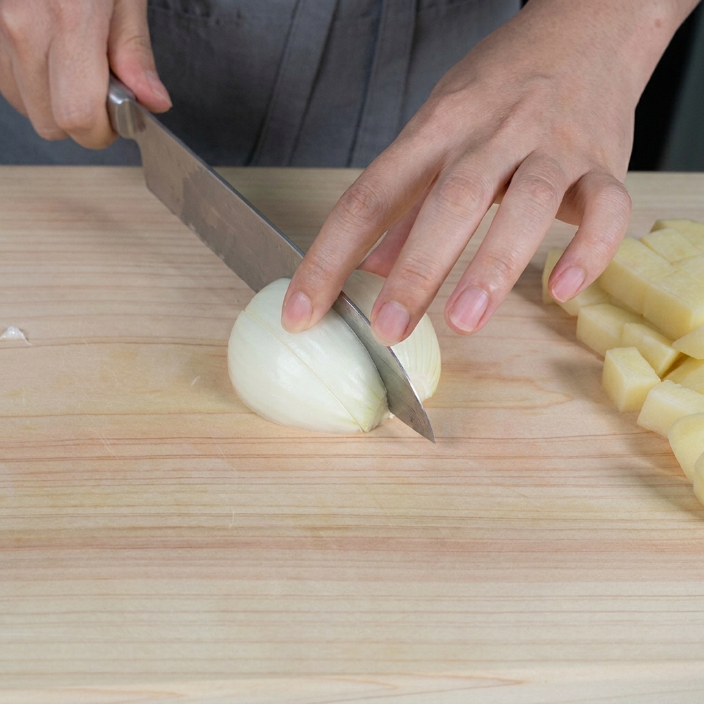 Hands chopping a raw white onion into small pieces on a light wooden cutting board.