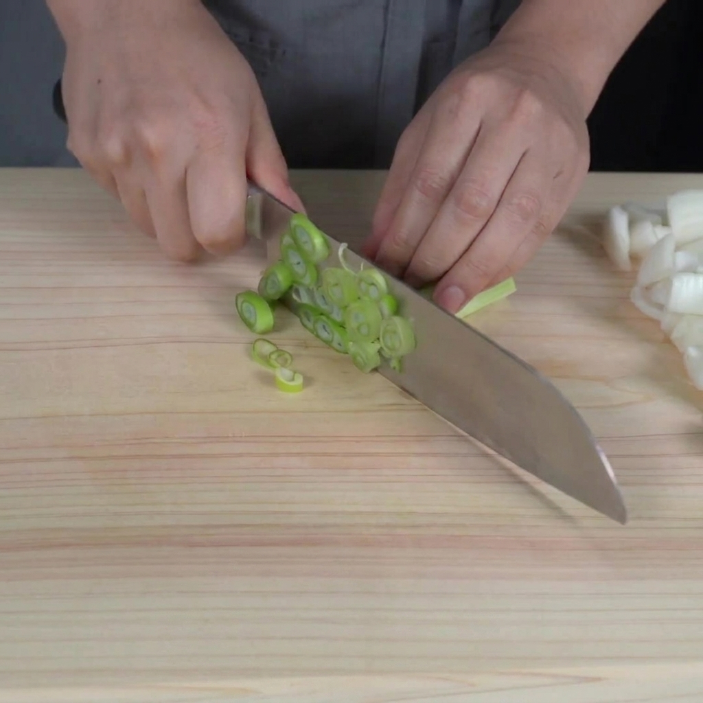 Slicing fresh green onions into small rounds on a wooden cutting board.