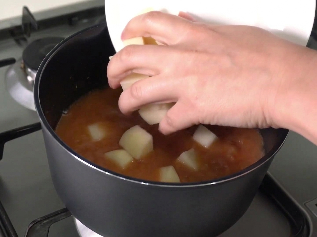Chopped potatoes and onions being slid from a white plate into a pot of boiling red broth.