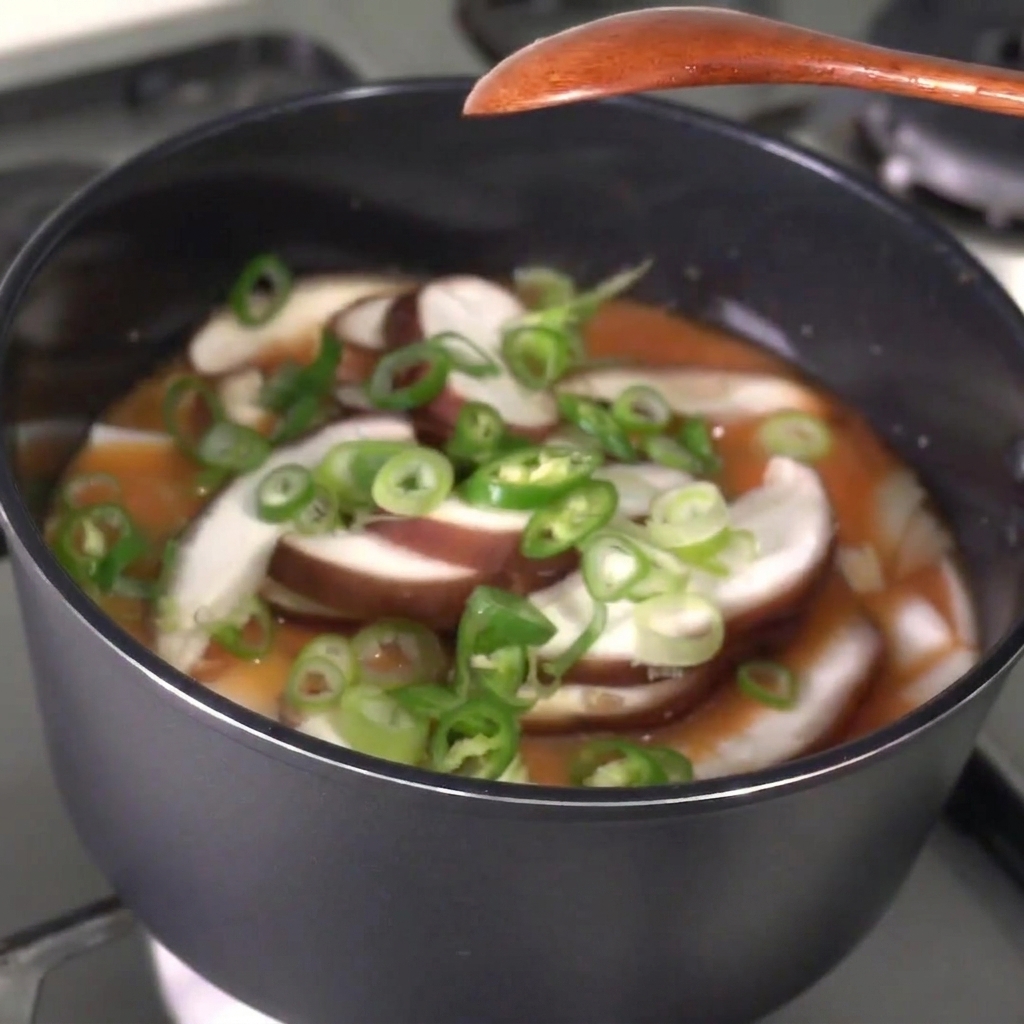 Sliced green chili peppers and green onions being sprinkled into a bubbling stew.