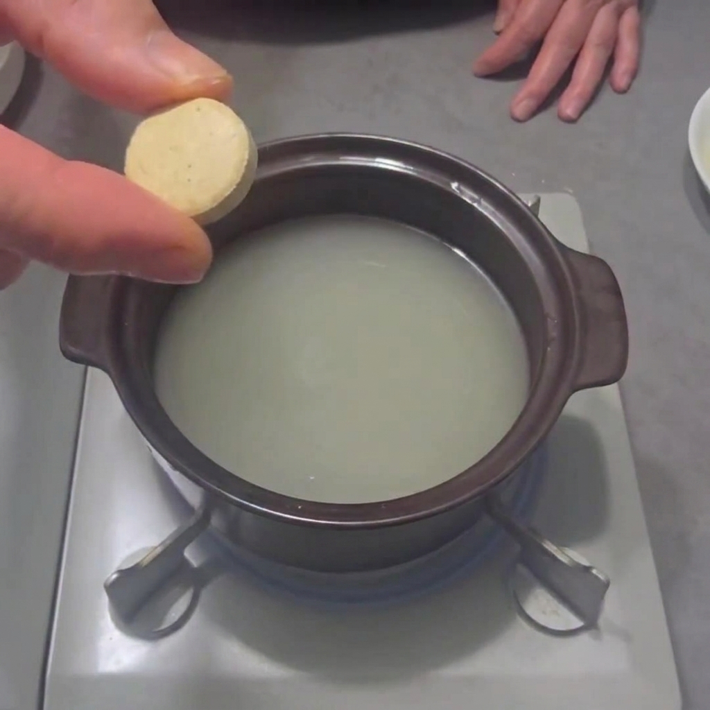 A seafood bouillon cube being dropped into a pot of water on a stovetop burner.