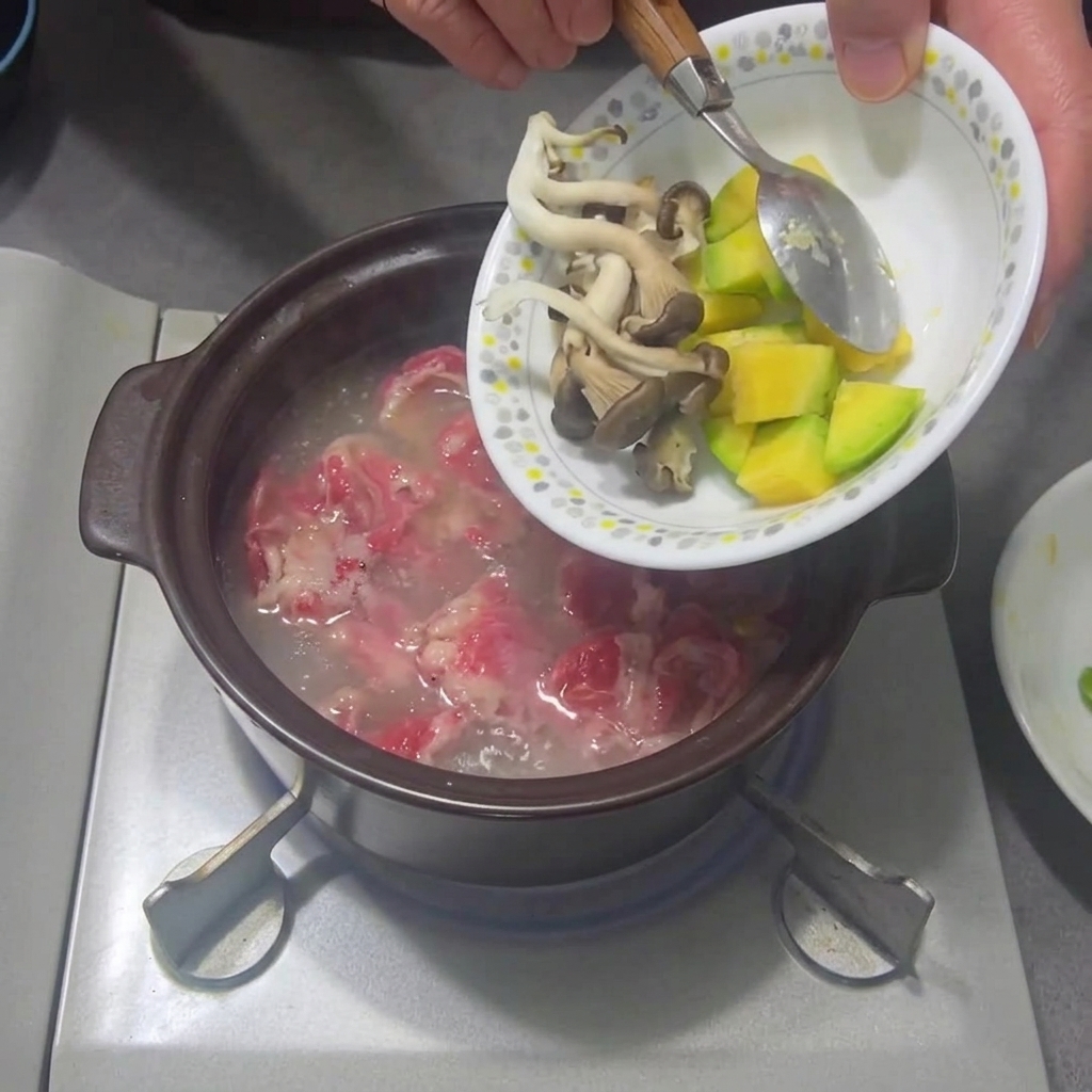Slices of mushrooms and zucchini being added to the simmering stew.