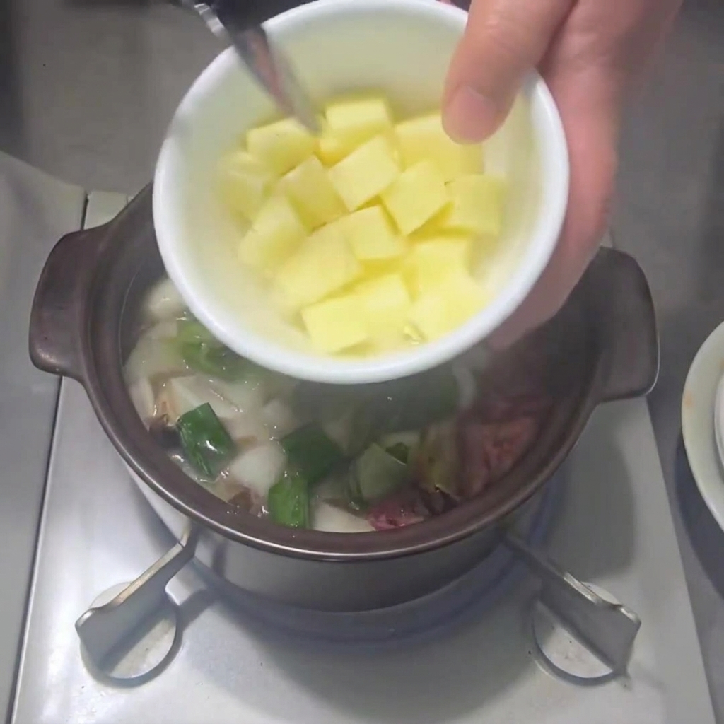 Diced potatoes being added to the pot with other vegetables.