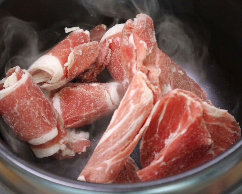 Thin beef brisket slices sizzling in a hot stone pot, releasing their own fat.