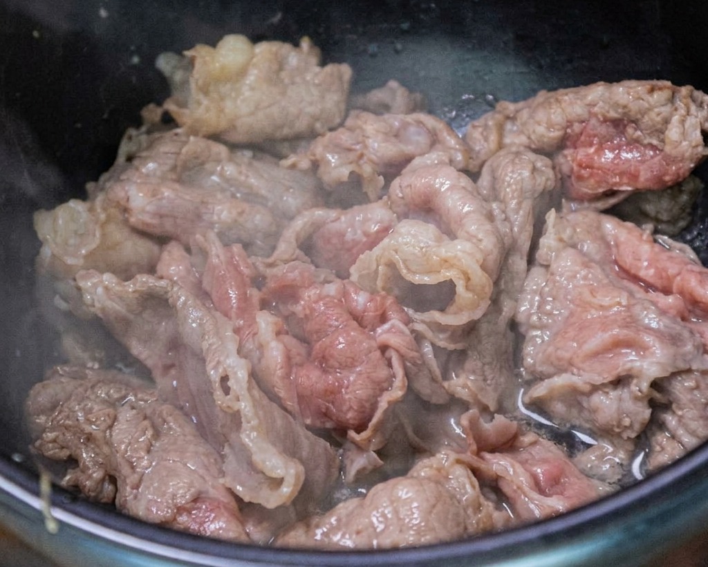 Beef being stir-fried in the pot with fresh minced garlic and green onions.