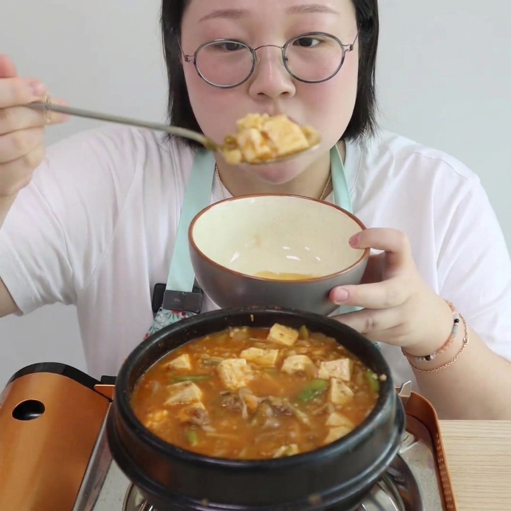 Cubed tofu and small sections of enoki mushrooms being added to the bubbling stew.