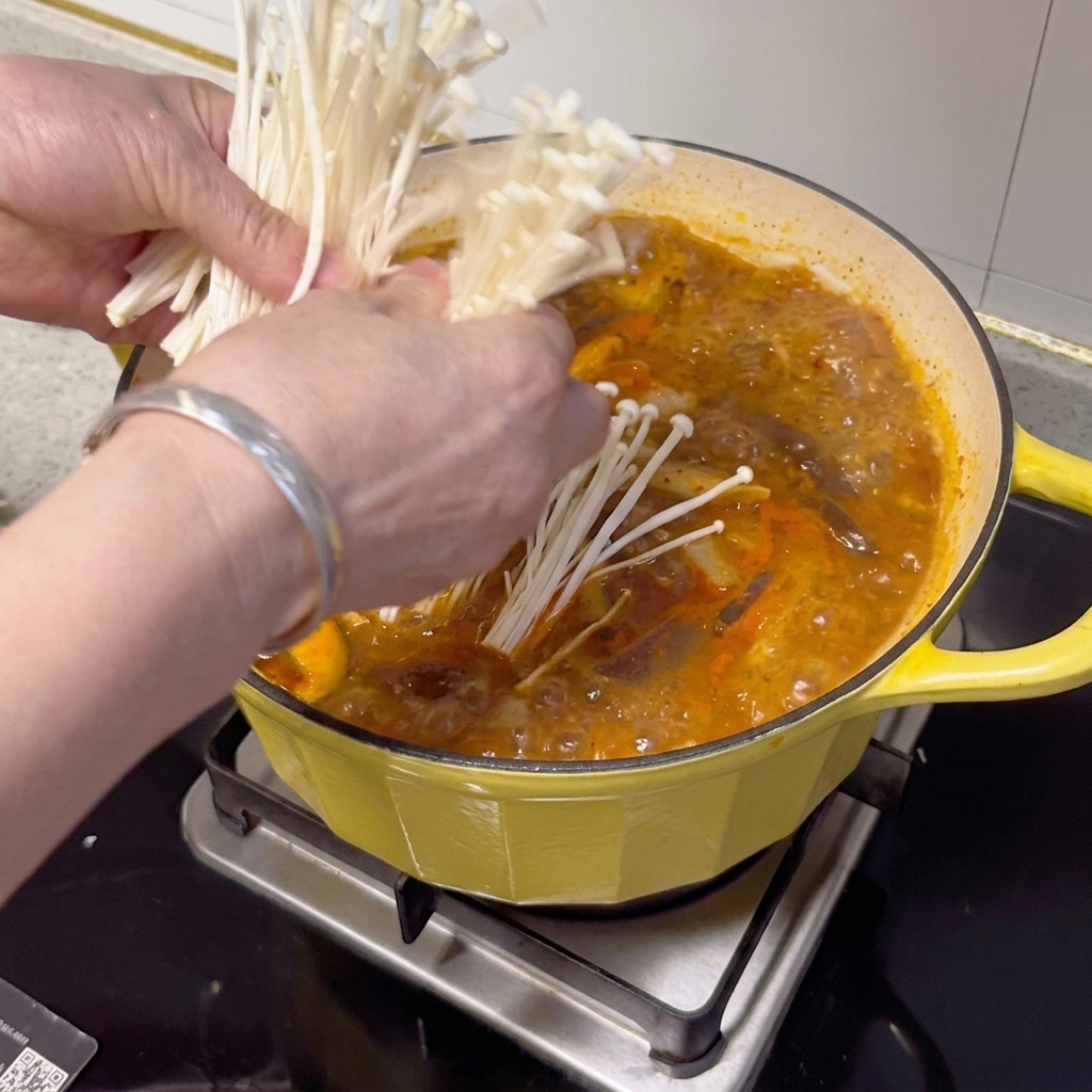 Fresh enoki mushrooms, green onions, and chili slices being arranged on top of the finished stew.