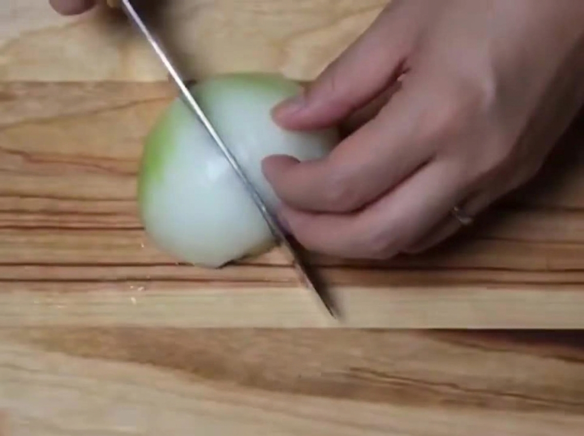 A white onion being chopped into small pieces on a wooden cutting board.