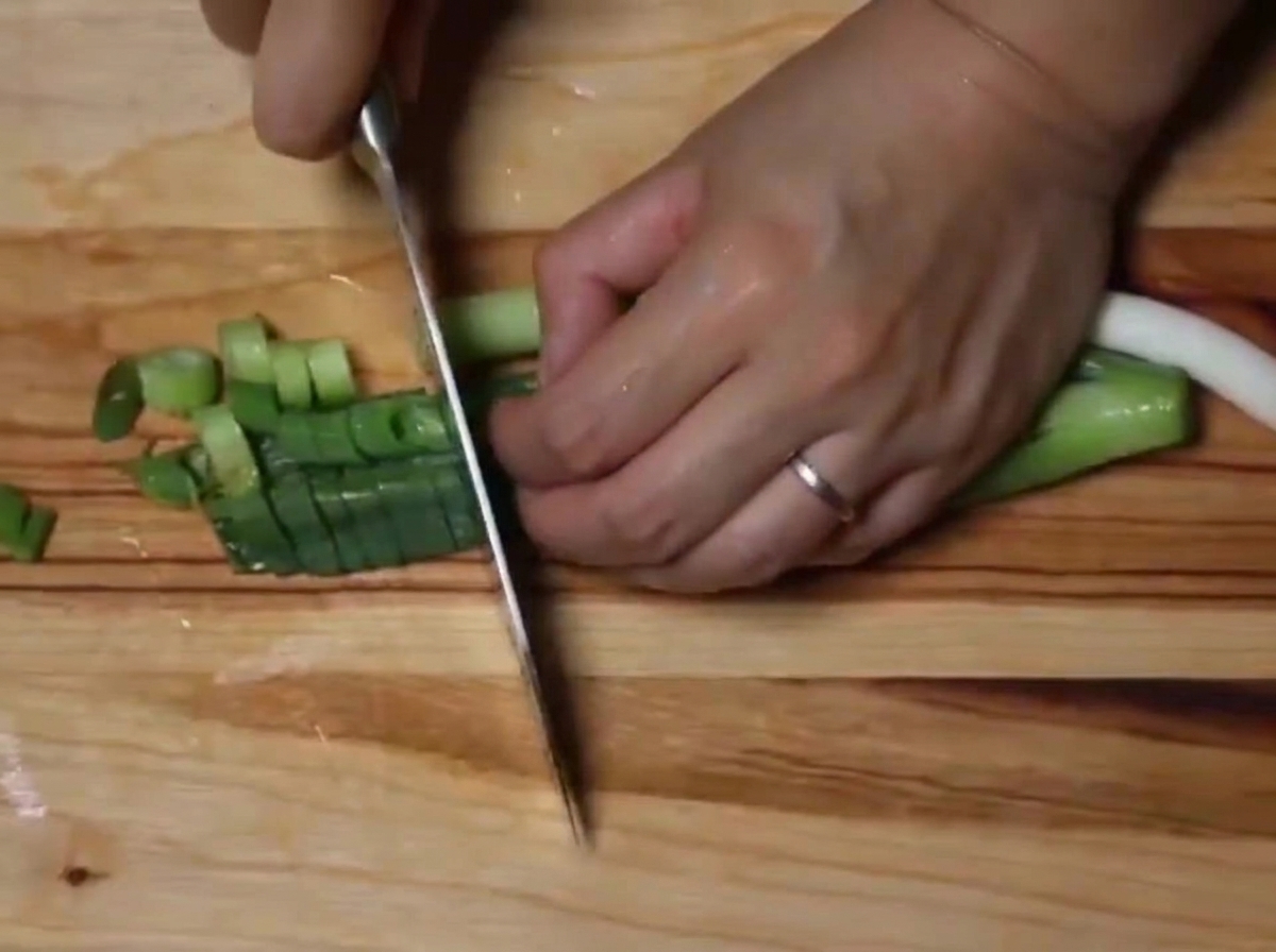 A close-up view of fresh green onions being sliced into small rounds on a wooden board.