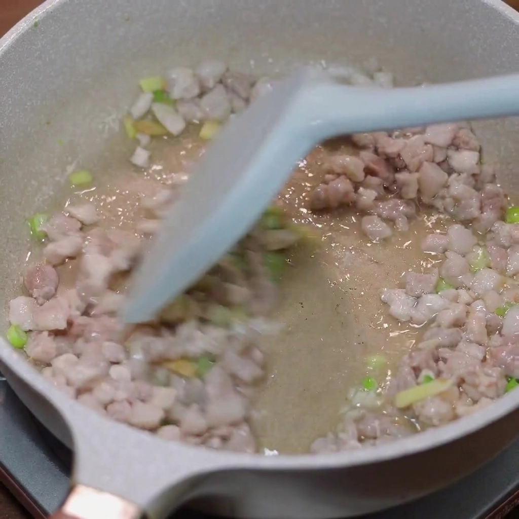 Minced pork being stir-fried in a pan with scallions and ginger.