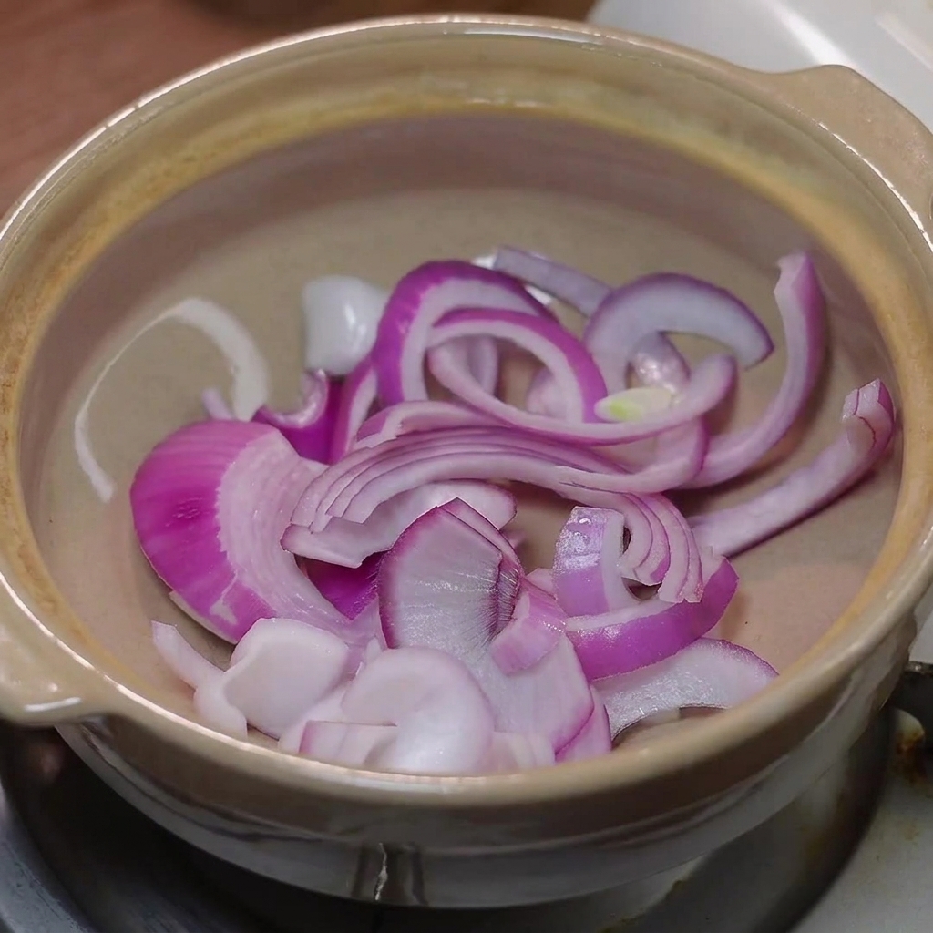 Sliced red onion and Napa cabbage placed in the bottom of a clay pot.
