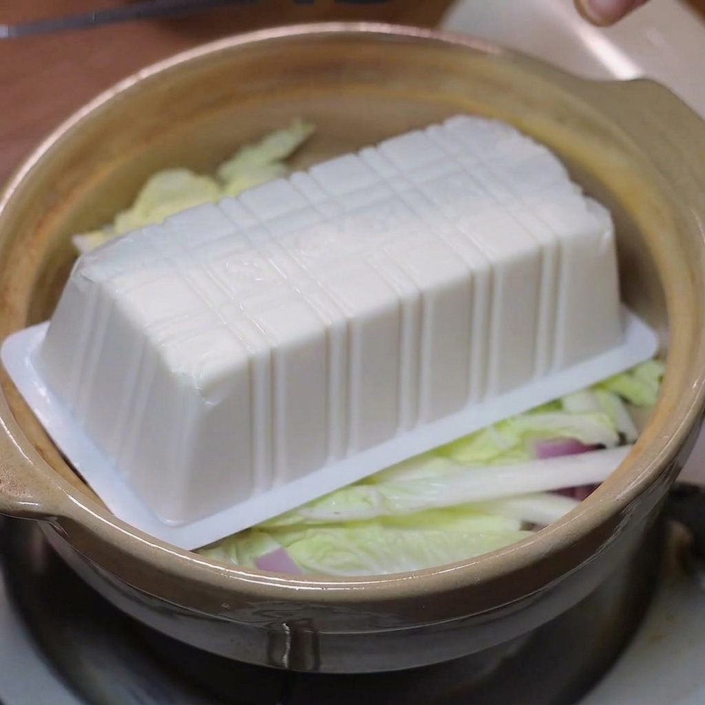 Soft tofu slices arranged on top of the cabbage and onions in the clay pot.