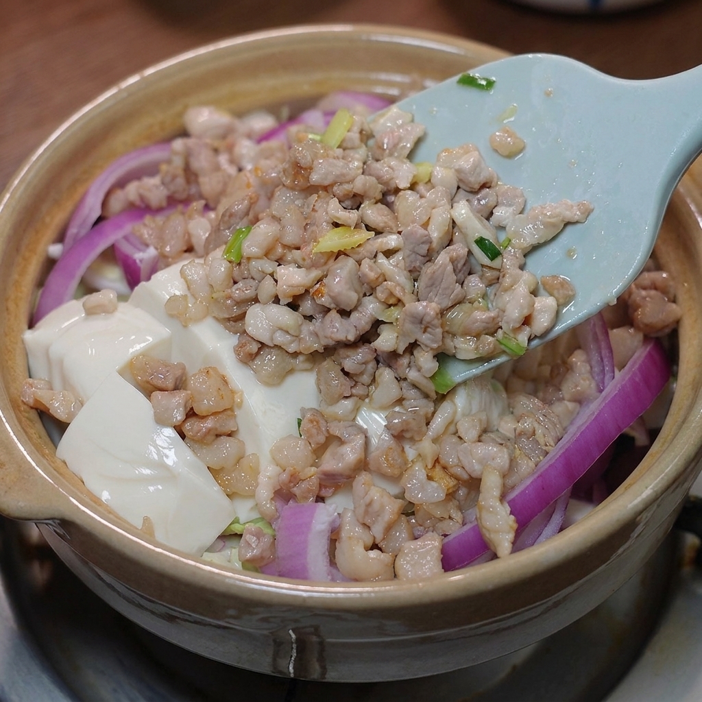 The stir-fried pork and prepared sauce being poured over the tofu in the clay pot.