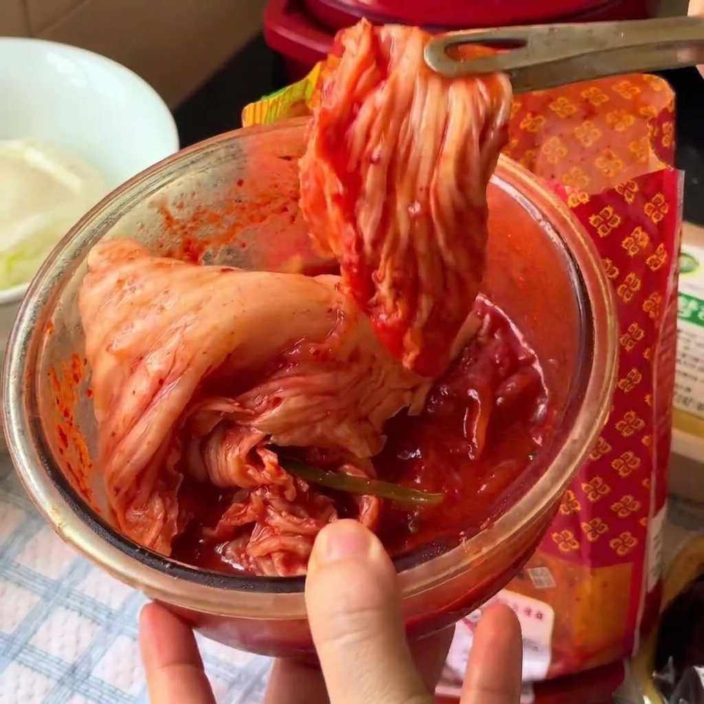 Kimchi being cut into smaller pieces inside a glass bowl using kitchen scissors.