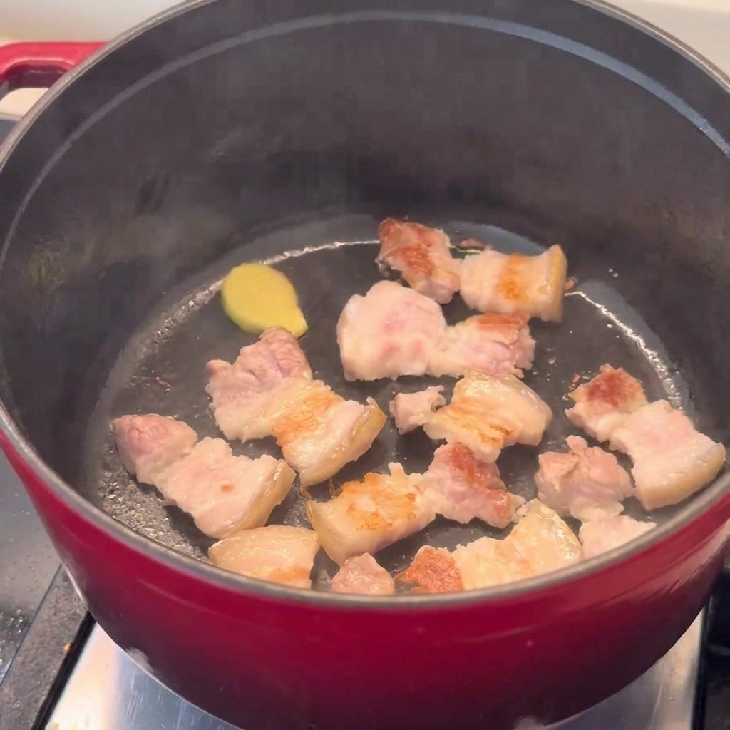 Golden brown pork belly pieces stir-frying in a red pot.