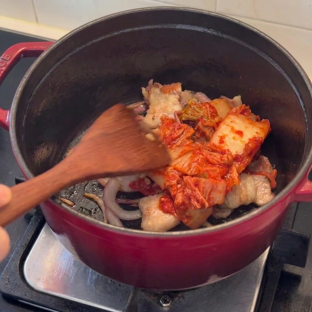Kimchi pieces being stir-fried together with seared pork belly in a pot.