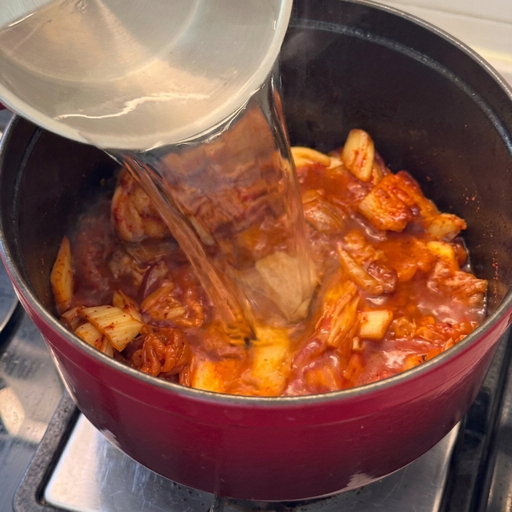 Water being poured into the pot with the pork and kimchi, beginning the stew base.