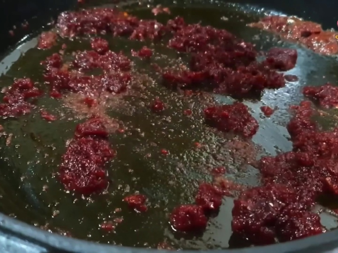 Small pieces of pork being mixed and stir-fried in a pan with a vibrant red chili-oil mixture.