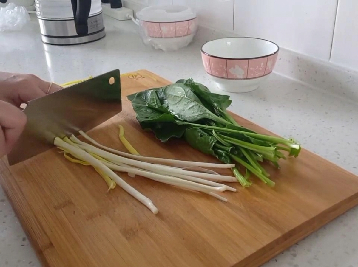 Close-up view of scallions being neatly sliced into small rounds on a wooden board.