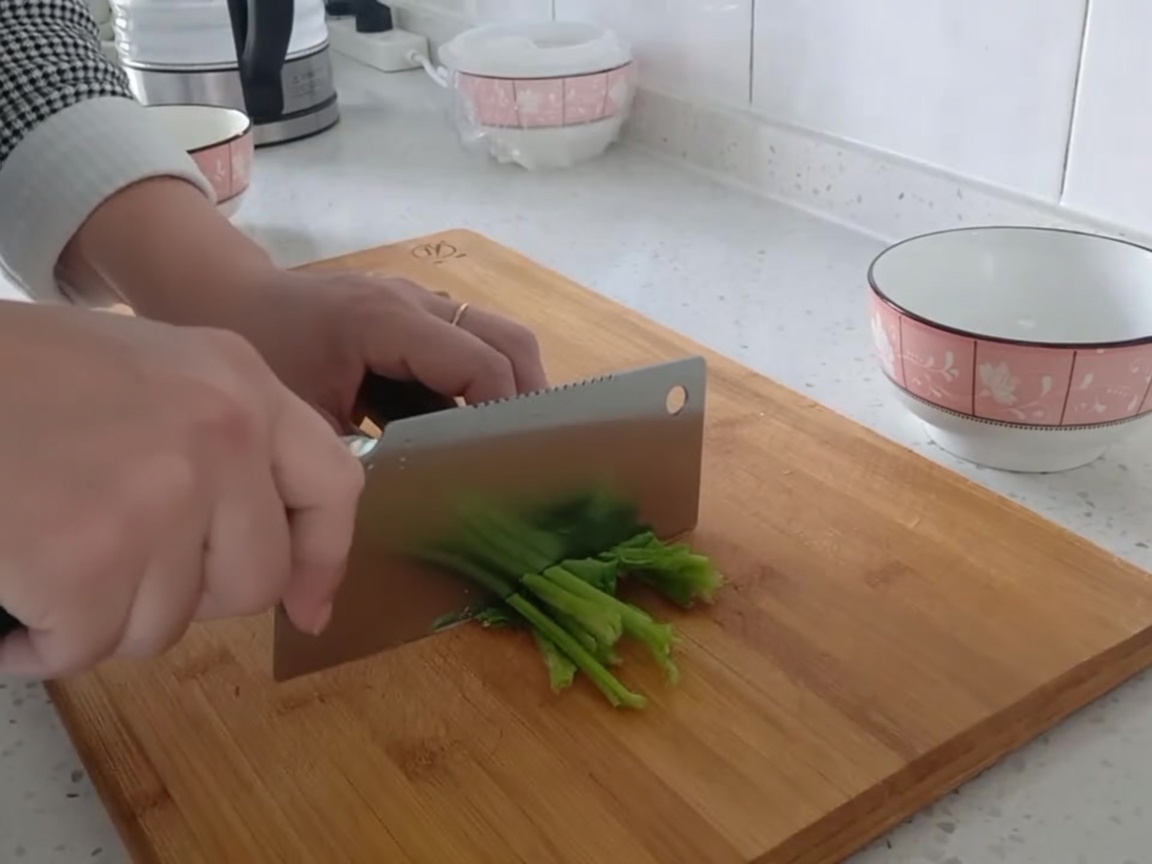 Fresh green spinach leaves being chopped into bite-sized pieces on a cutting board.