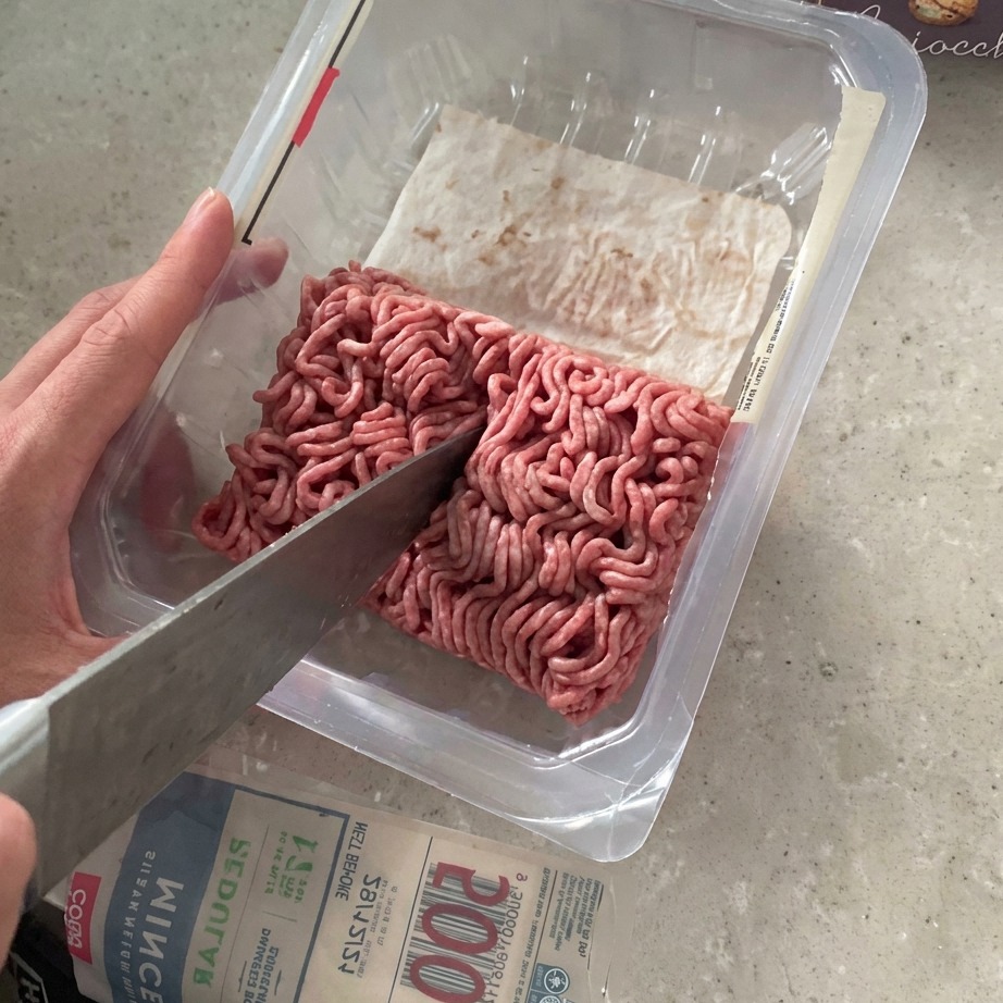 Ground beef being cut in half with a large knife inside its supermarket packaging.