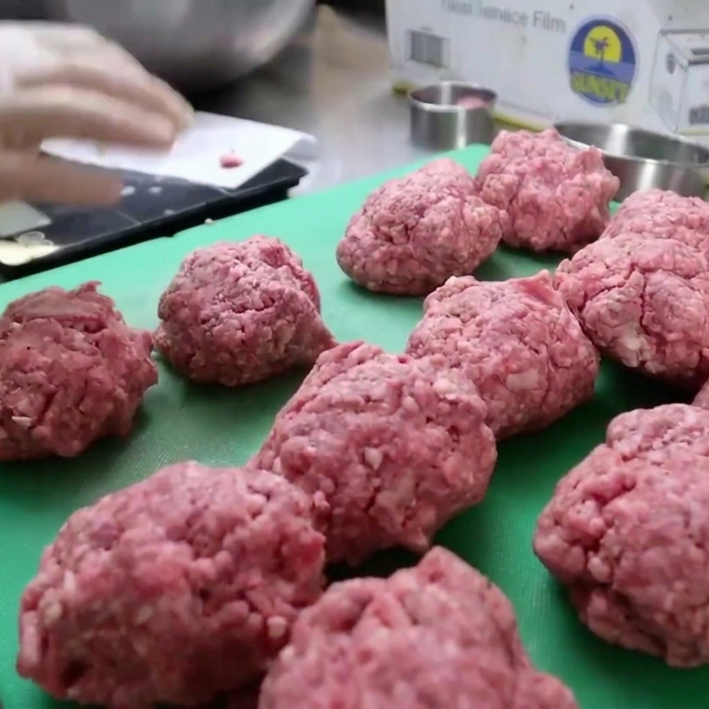 Ground bison meat being packed into a circular mold to form thick burger patties.