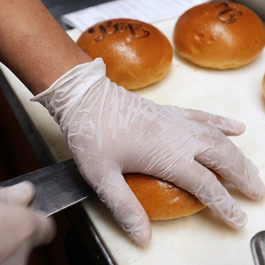 Burger buns being sliced open and coated with butter for the grill.